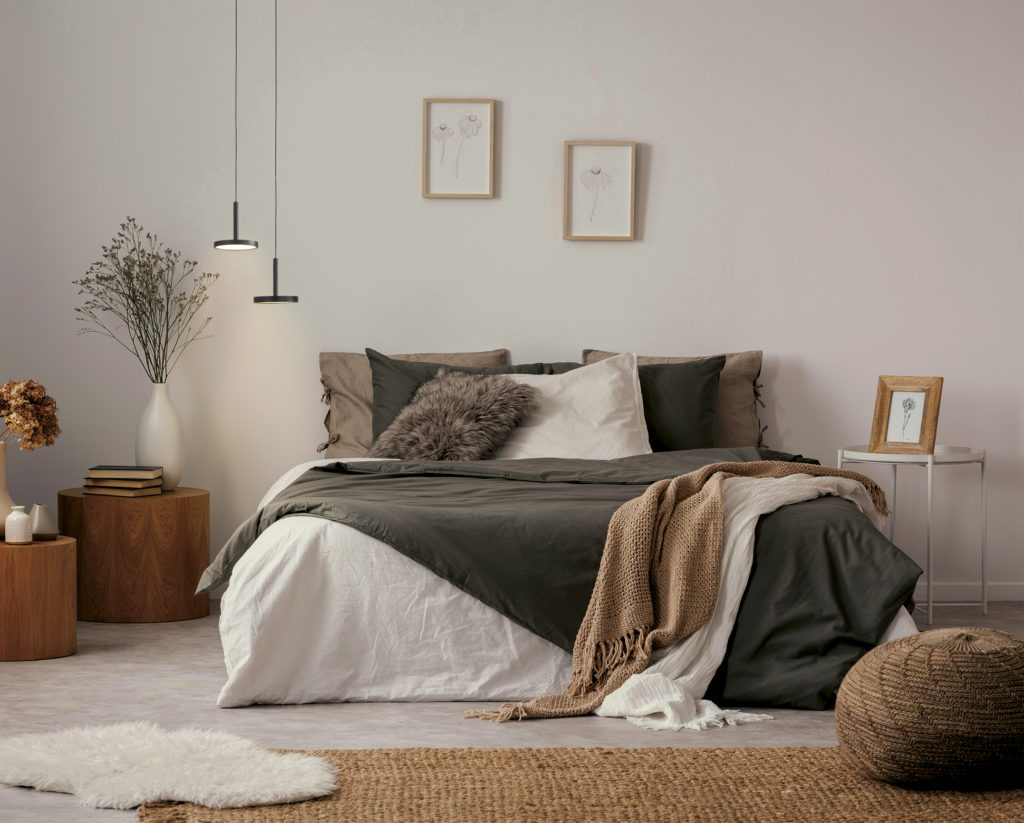 Flowers on wooden stool and pouf in white bedroom interior with