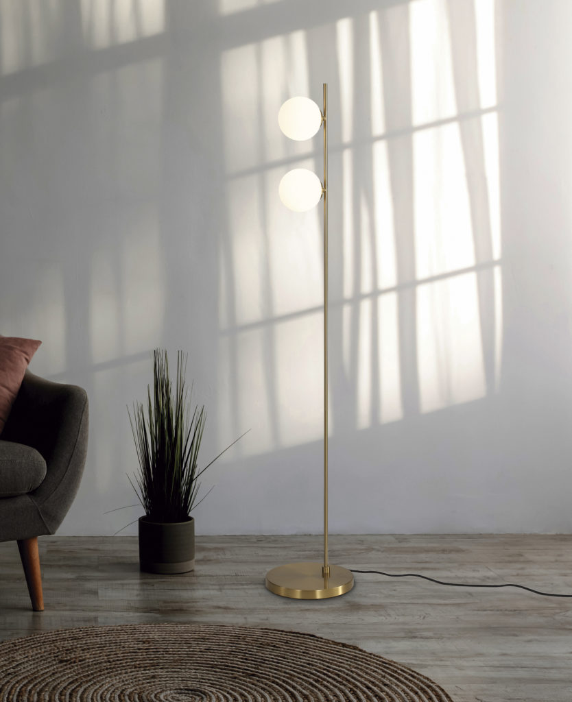 Cozy armchair with pillow, luminous lamp on table, potted plant, ottoman and round carpet